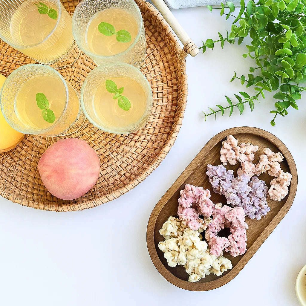 Happy Munch Factory yogurt clusters—assorted fruit flavors on a wooden tray beside iced drinks and a peach, overhead.