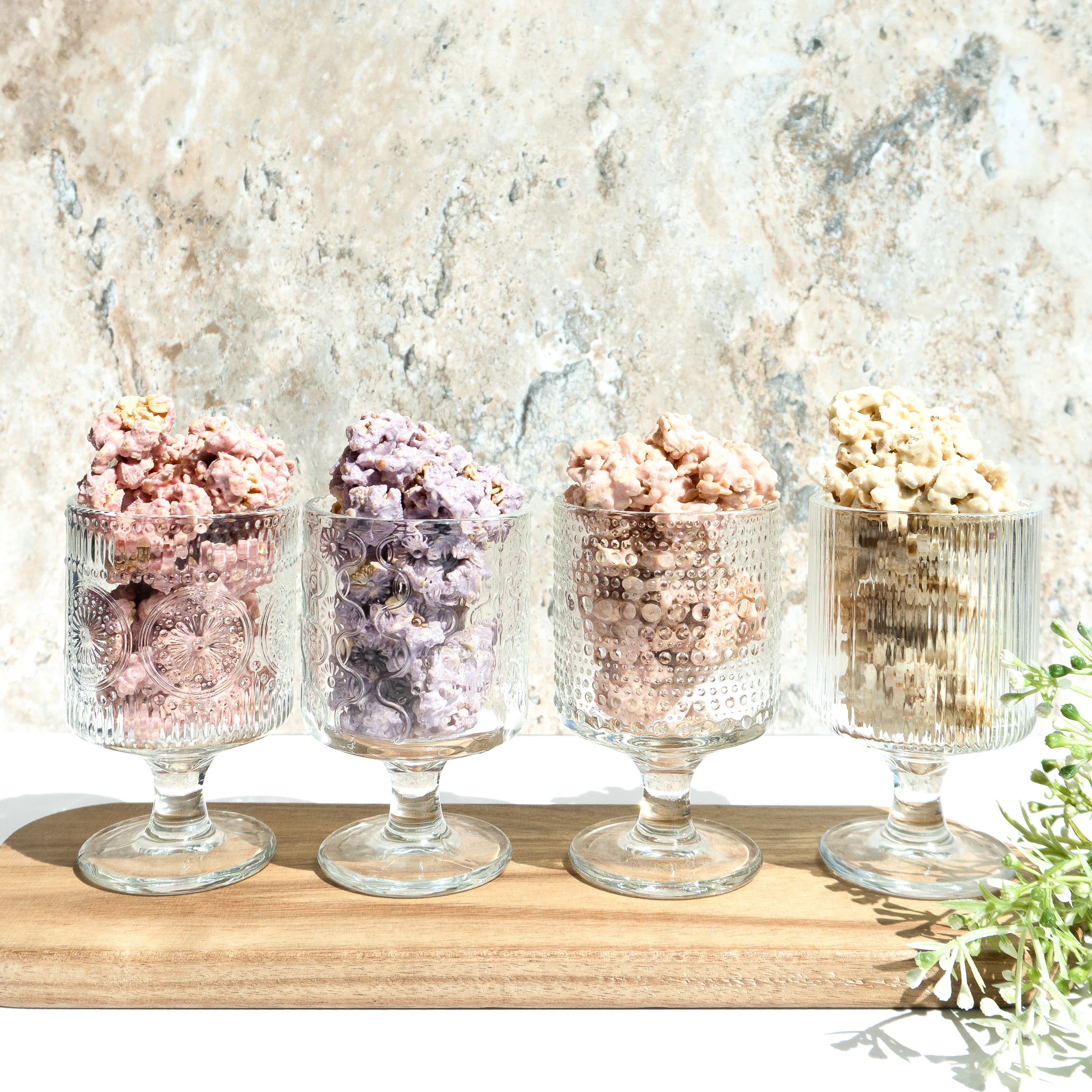 Happy Munch Factory yogurt clusters—four flavors displayed in glass cups on a wooden board.