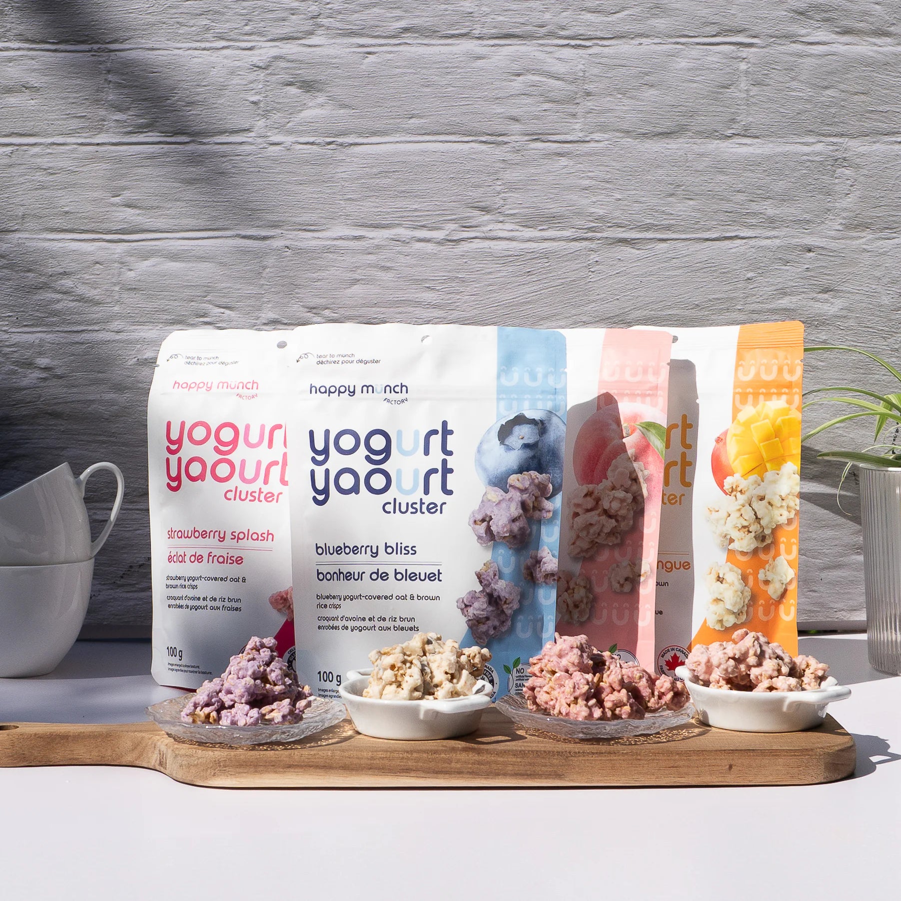 Happy Munch Yogurt cluster packages with samples on a wooden board against a gray textured wall.