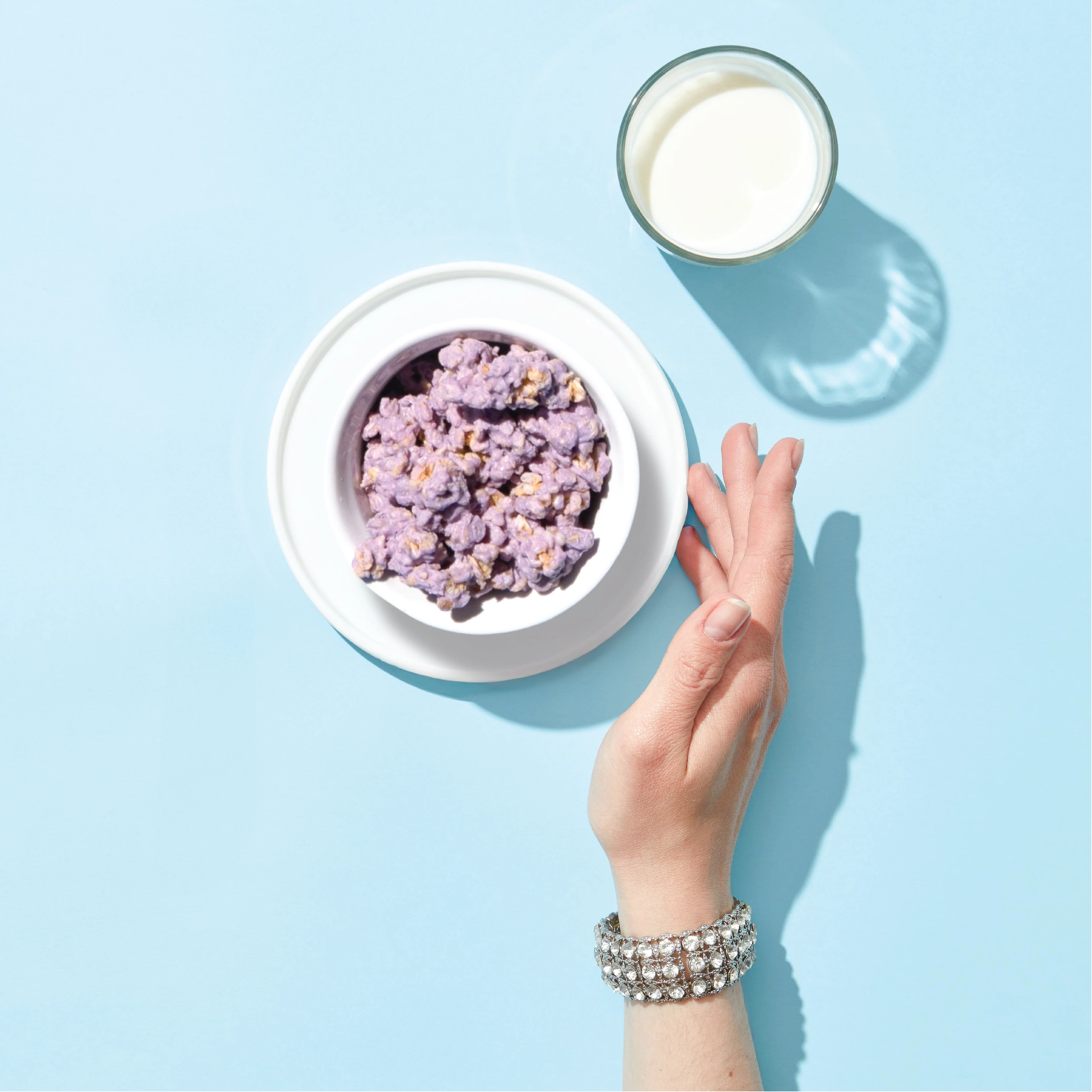 Bowl of Happy Munch Blueberry Bliss  with a glass of milk on a light blue background