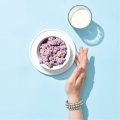Bowl of Happy Munch Blueberry Bliss  with a glass of milk on a light blue background
