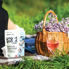 Happy Munch Blueberry Bliss Yogurt cluster package with a picnic setup including a basket with flowers and a glass of pink drink.