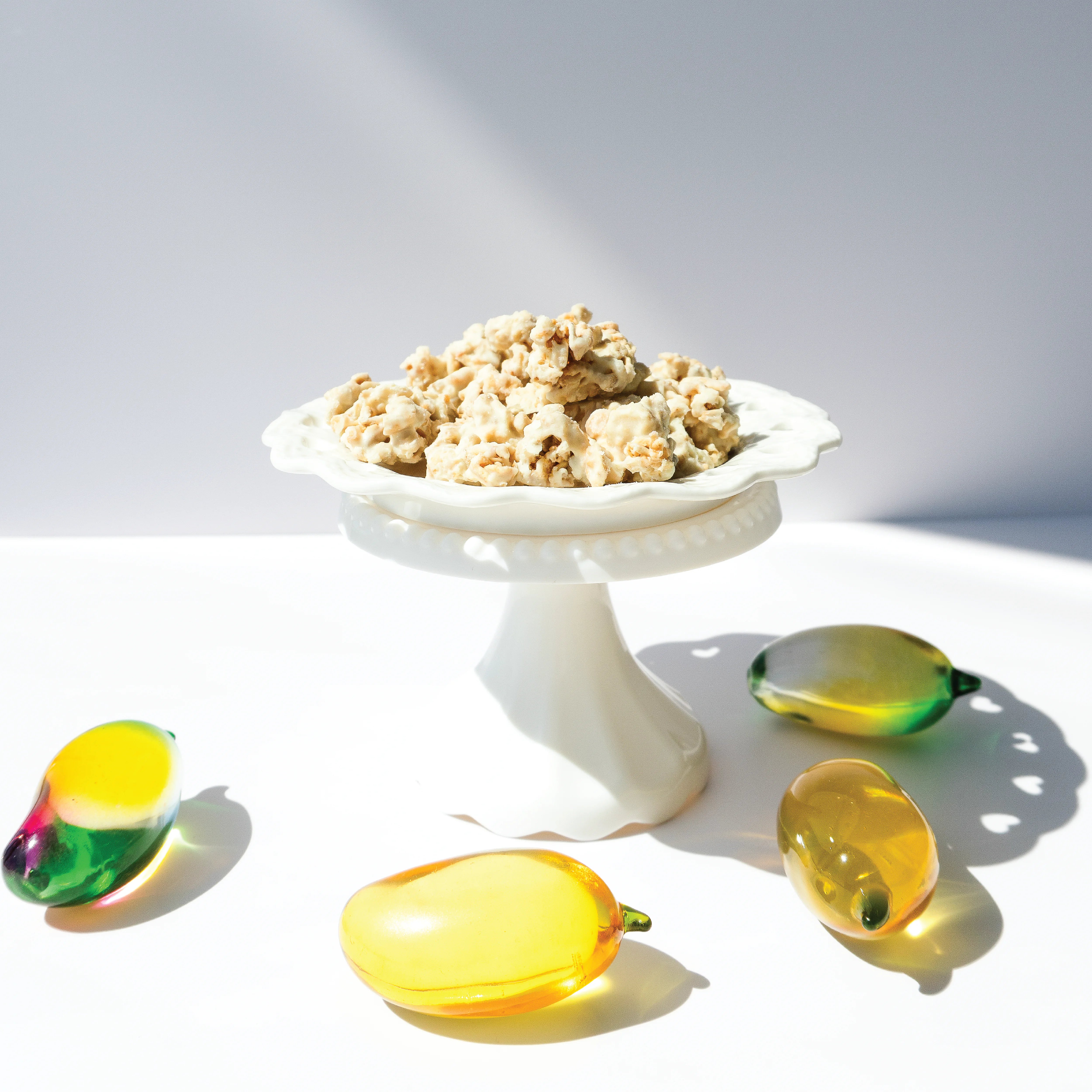 Happy Munch Mango Mania clusters on a white decorative plate surrounded by glass mangos.