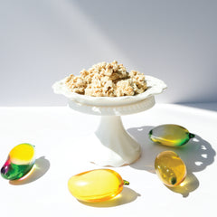 Happy Munch Mango Mania clusters on a white decorative plate surrounded by glass mangos.