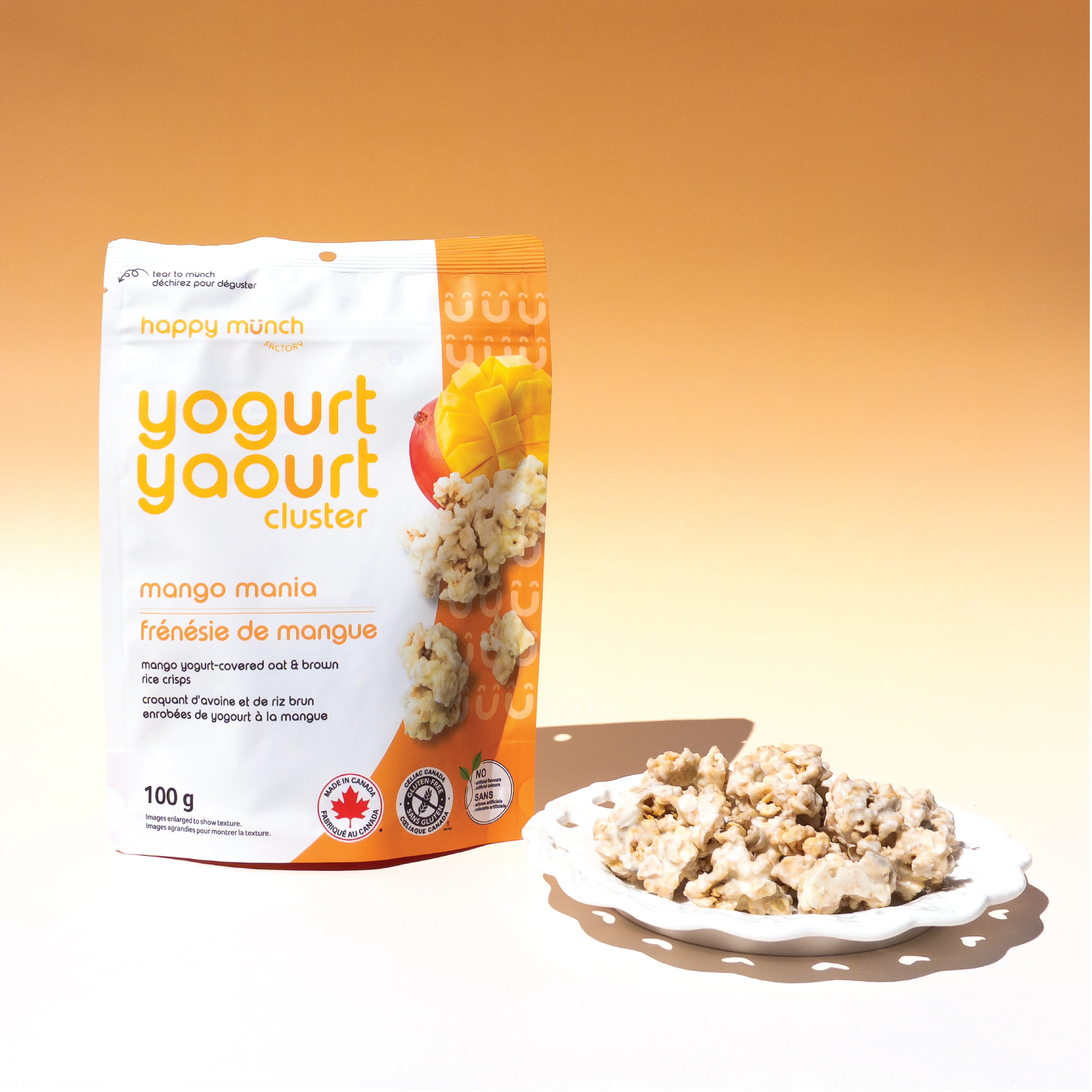 Happy Munch Mango Mania yogurt cluster package with a plate of Yogurt Clusters on an orange background
