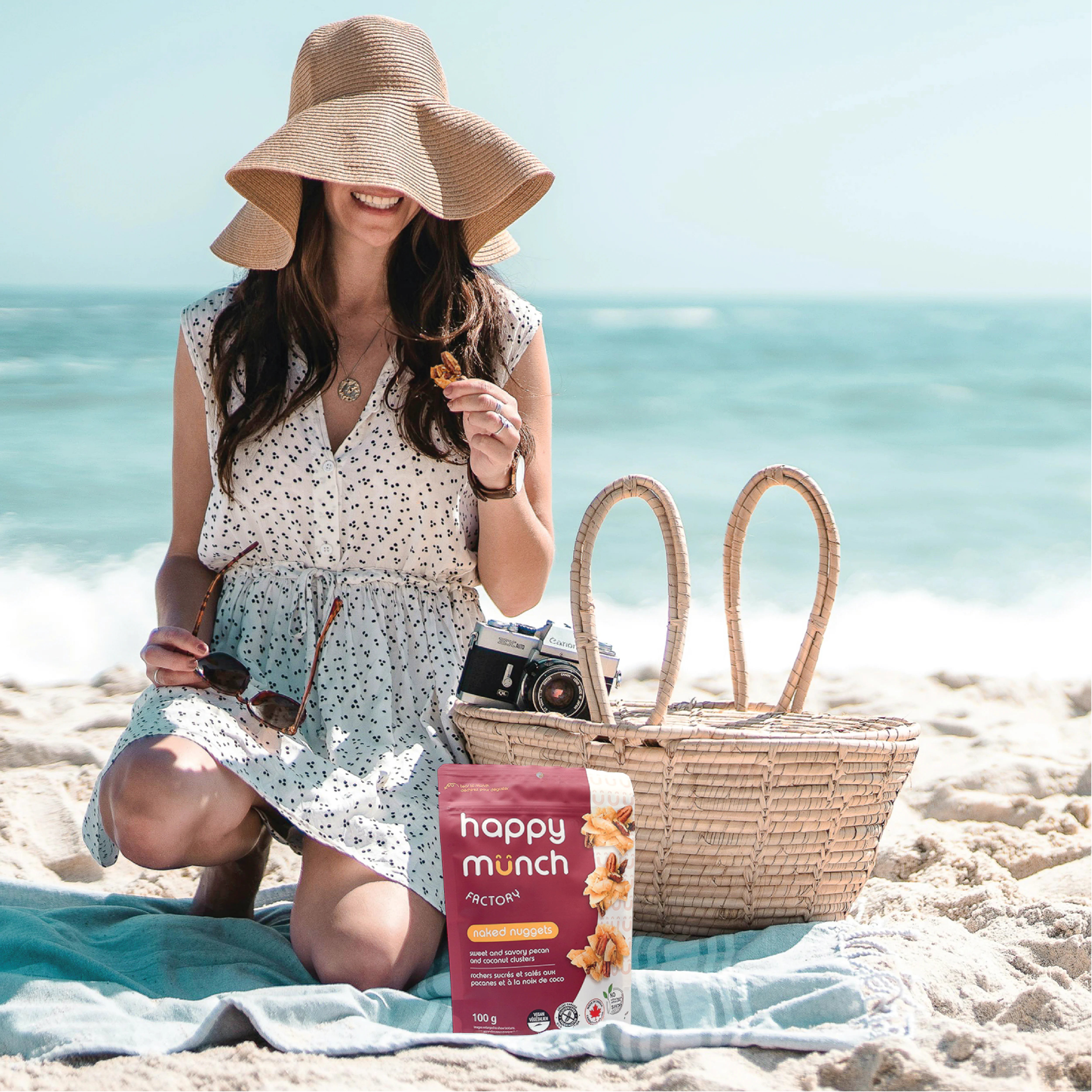 Woman on a beach with a 'Happy Munch Naked Nuggets' snack package and picnic basket