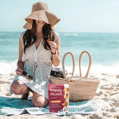 Woman on a beach with a 'Happy Munch Naked Nuggets' snack package and picnic basket