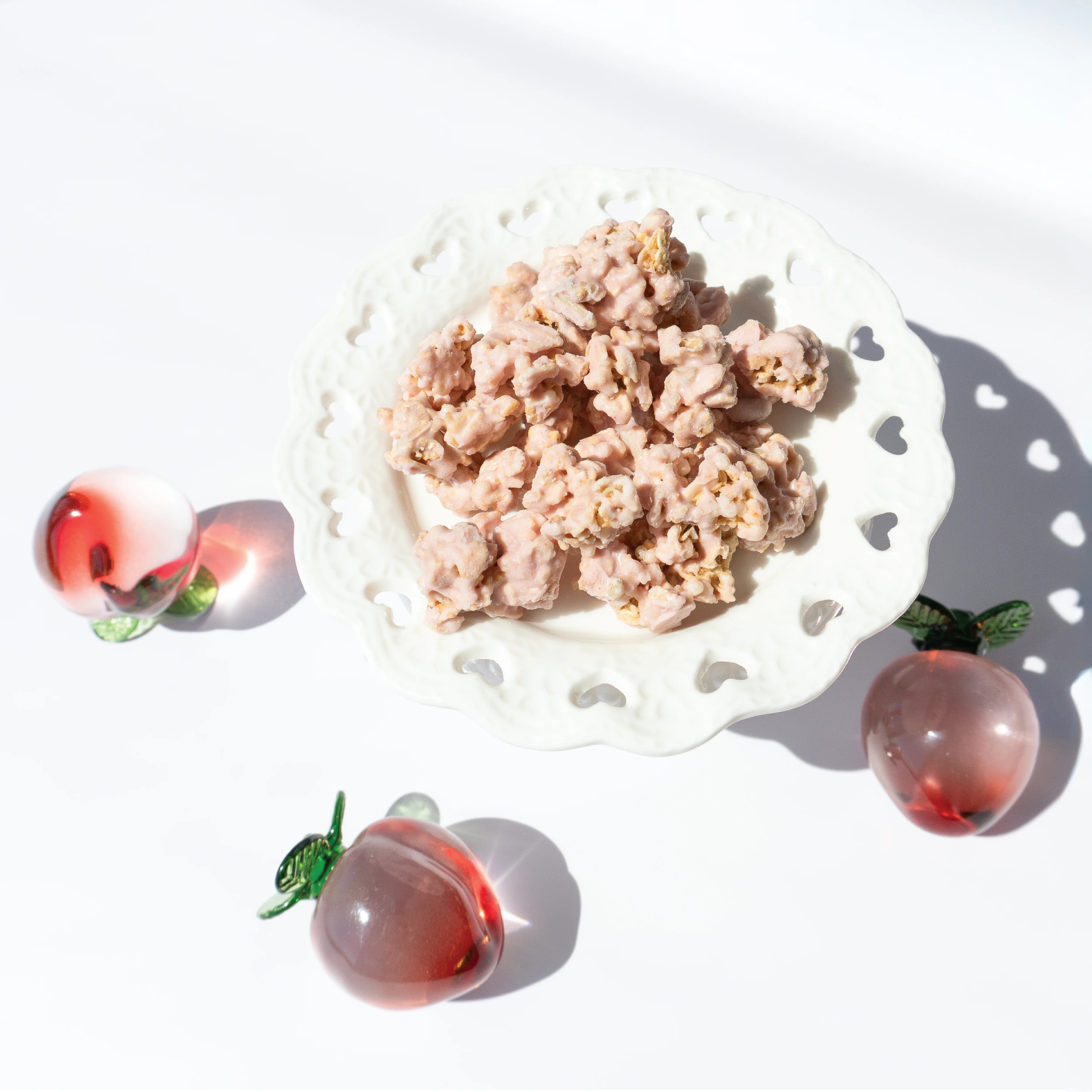 Happy Munch Peach Paradise Yogurt Clusters on a white decorative plate with 3 glass peaches.