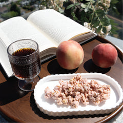 Glass of coffee peaches, and a plate of Happy Munch Peach Paradise clusters on a wooden table with an open book.